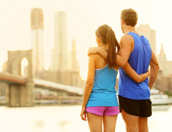 Fitness couple relaxing after running in Brooklyn, New York City, USA. Happy sporty fit young interracial couple enjoying view of Brooklyn Bridge after jogging training outside. Woman and man in 20s.