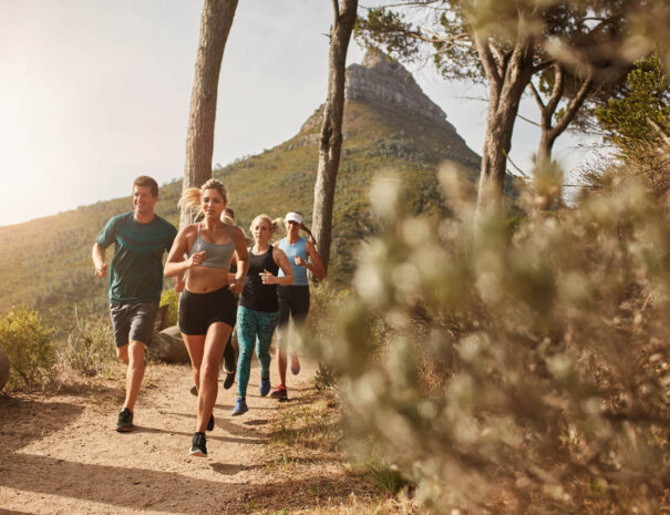 Group of young adults training and running together through trails on the hillside outdoors in nature. Fit young people trail running on a mountain path.