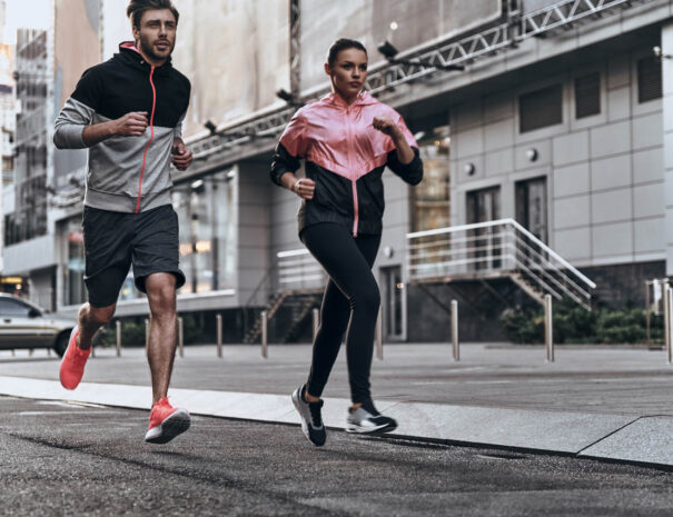 Out for a run. Full length of young couple in sport clothing running through the city street together